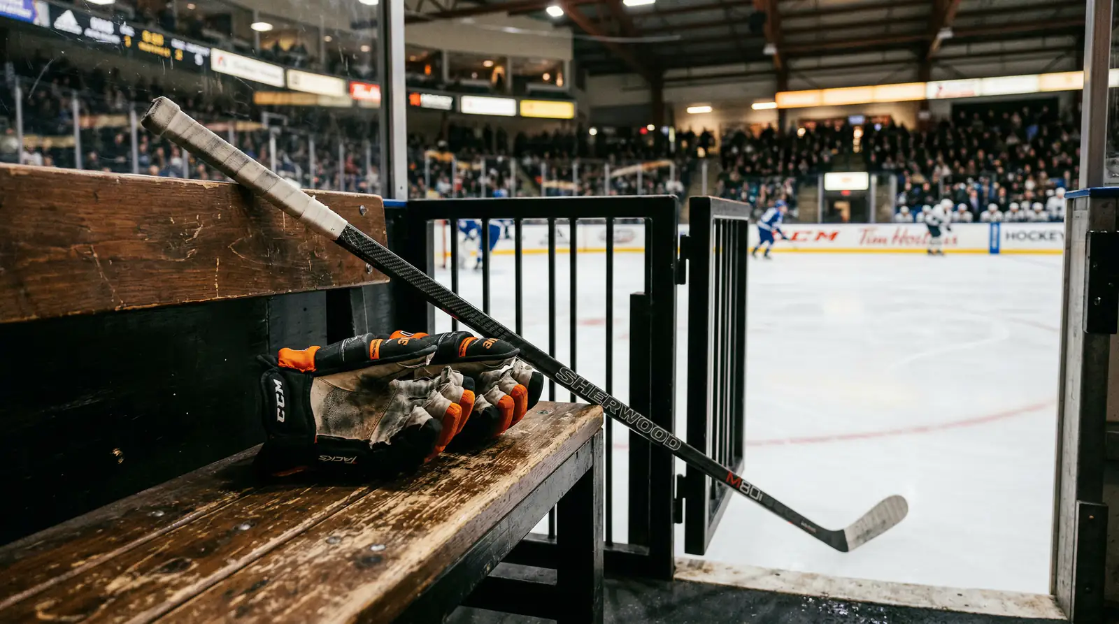 Eishockey-Handschuhe und Schläger auf einer Bank neben der Eisfläche